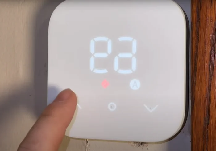 Main réglant un thermostat numérique sur une température confortable